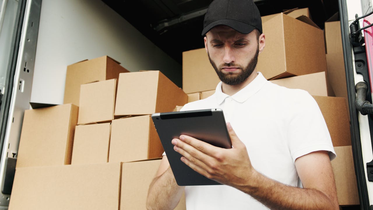 portfolio-05 Delivery worker using a tablet to manage shipments with stacked boxes in the background.