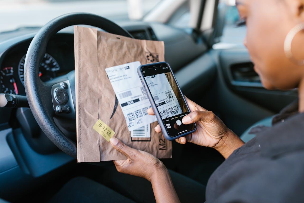 portfolio-01 Close-up of a courier in a car scanning a package label with a smartphone for delivery service.