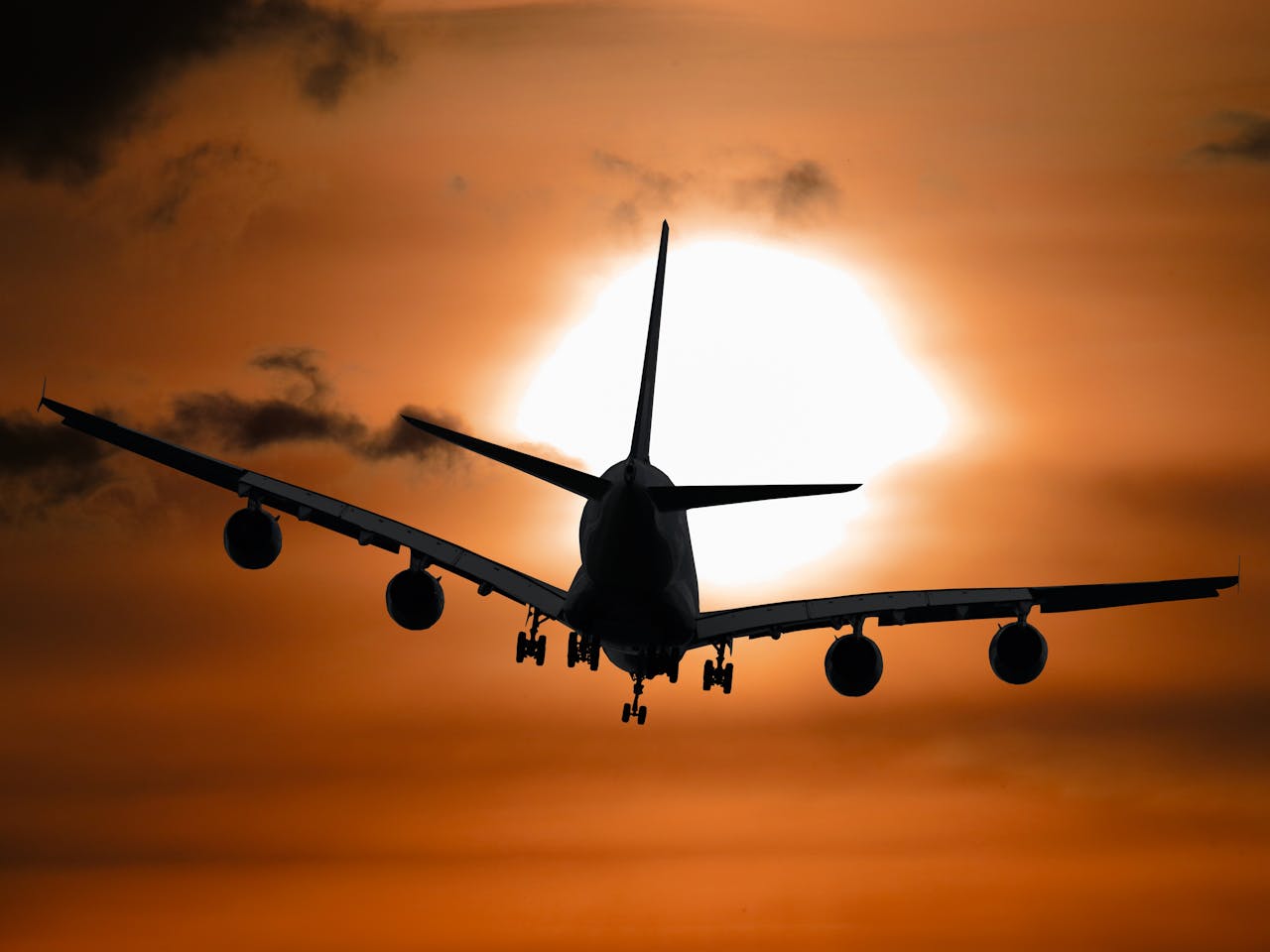 why-choose-us Dramatic silhouette of an airplane flying against a vibrant sunset sky.